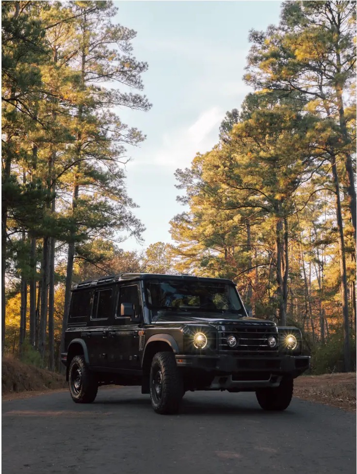 Dark off-road wagon on a narrow road framed by tall pines