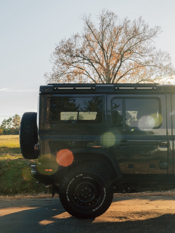 Rear quarter of a dark off-road wagon with sun flare and autumn tree