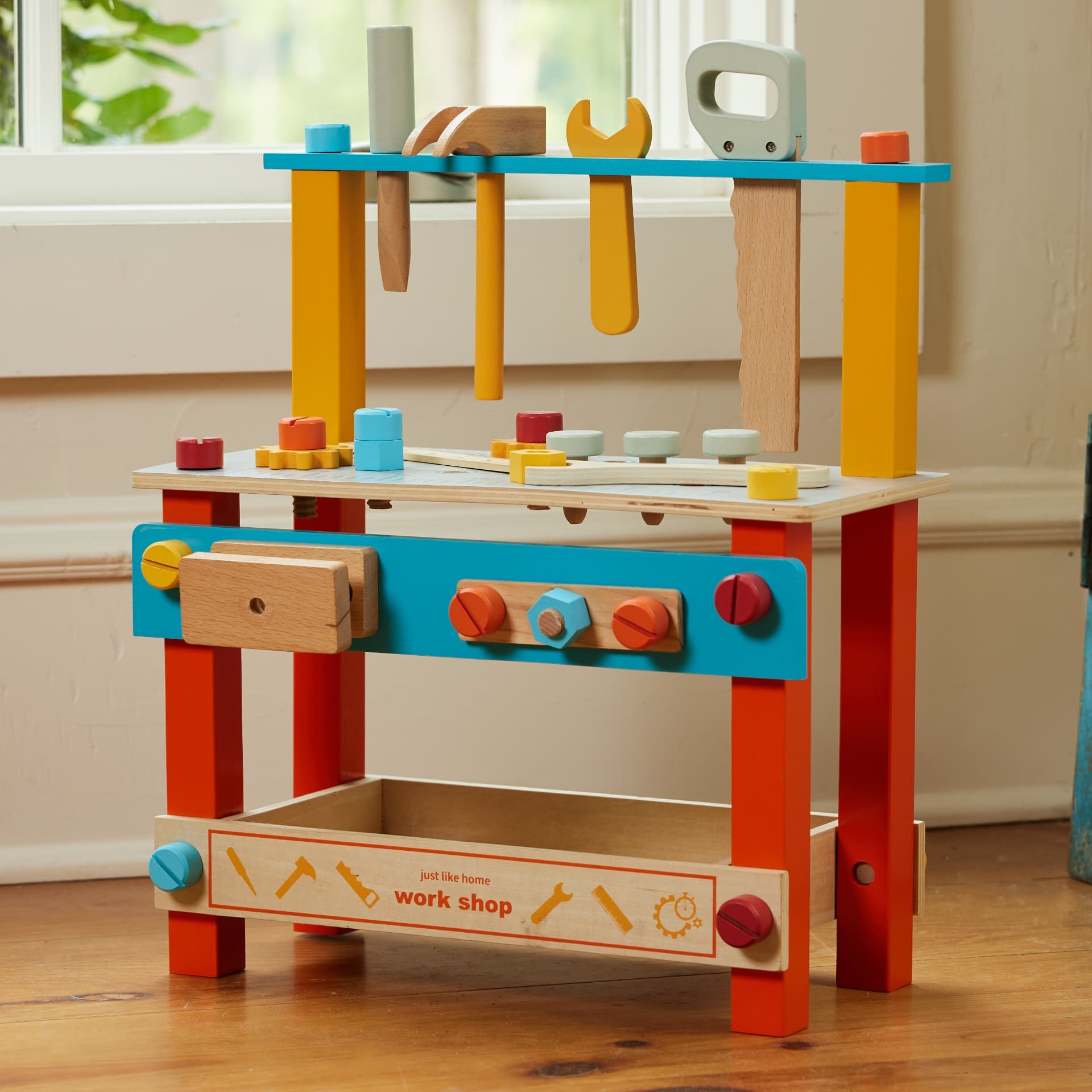 Brightly painted wooden toy workbench with miniature tools by a sunlit window