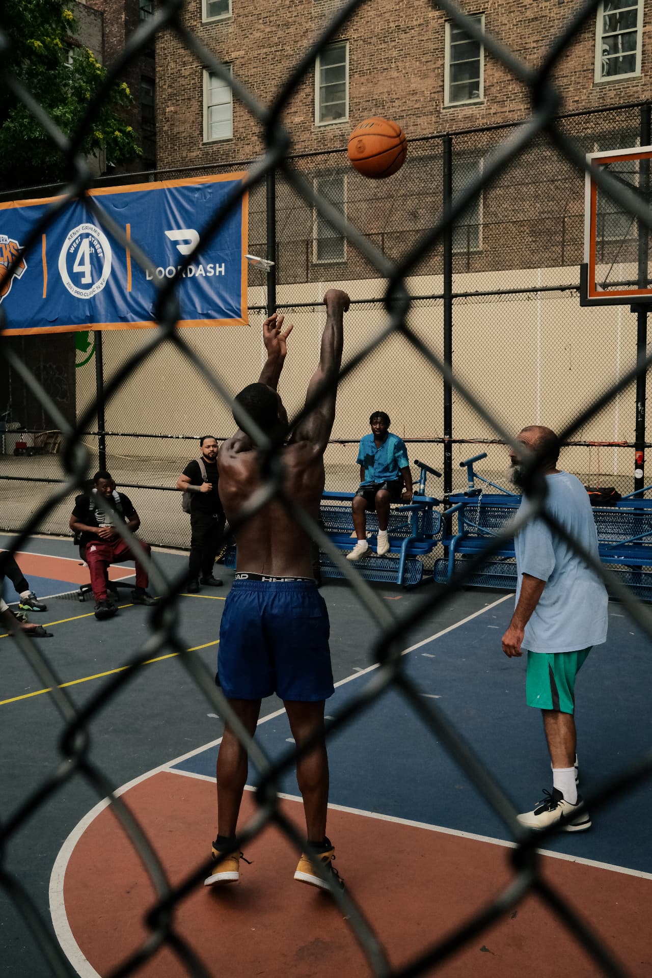 Basketball game seen through chain link fence at the West 4th Street court