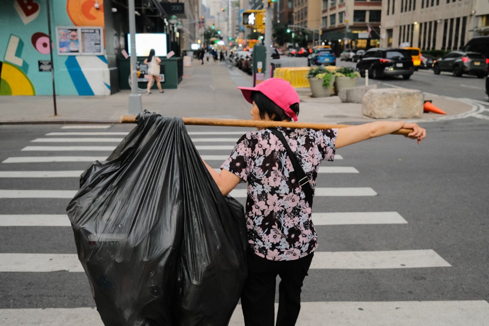 Worker carrying bagged recycling on a pole across a Manhattan crosswalk